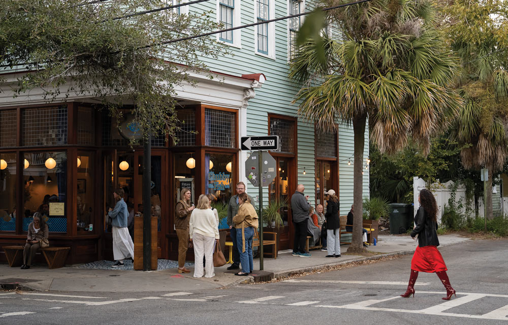 A lively café on a street corner with people gathered outside and a woman crossing the street.