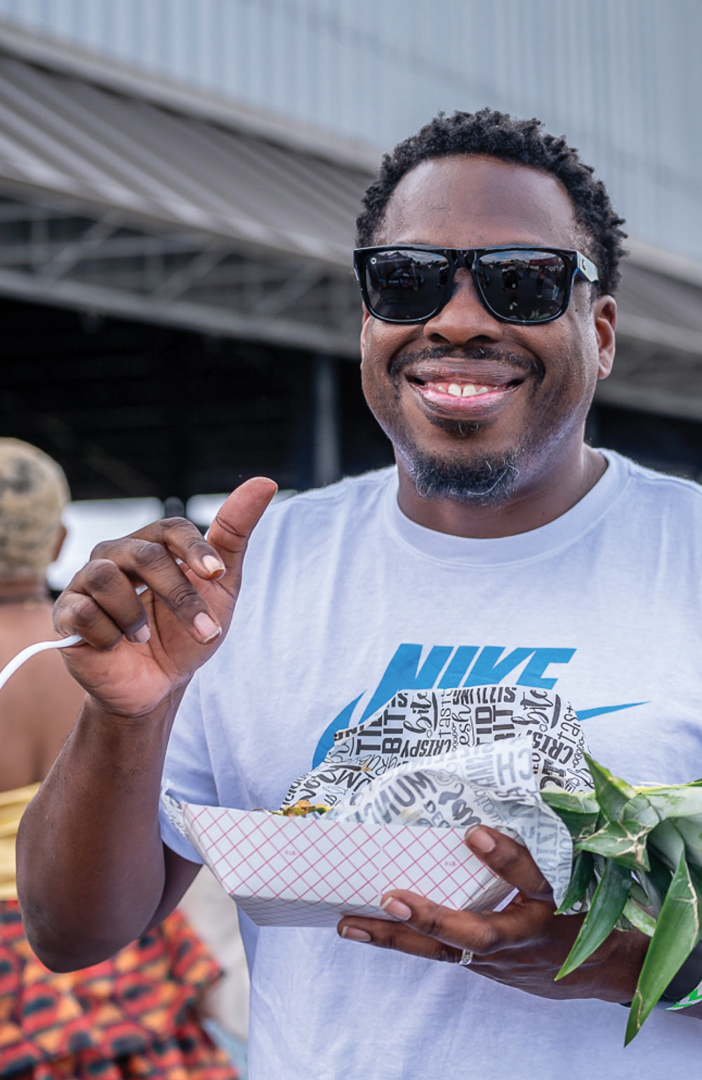 Man smiling while holding a food tray and a pineapple top.