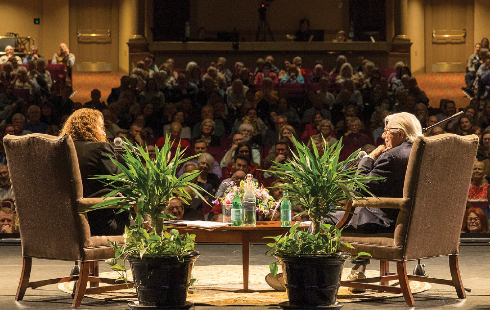 two people sitting in chairs on stage in front of audience for interview