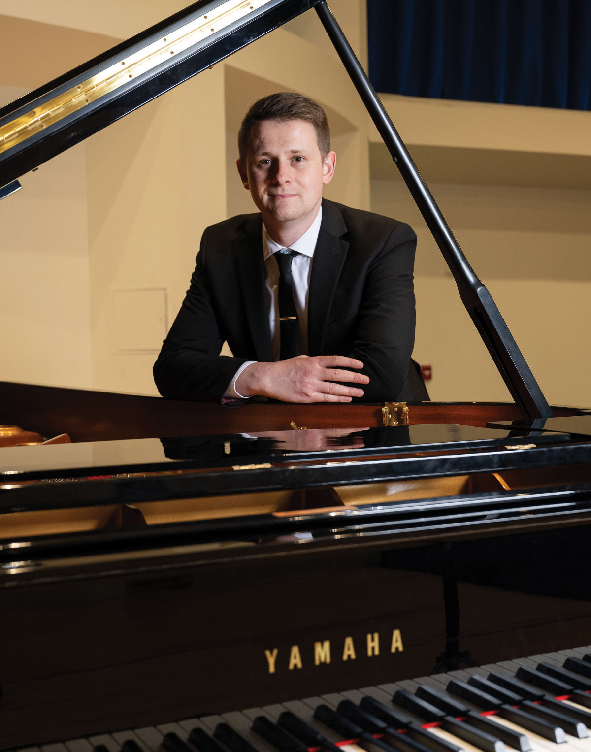 Tom Hicks leaning forward on a piano to pose for a photo