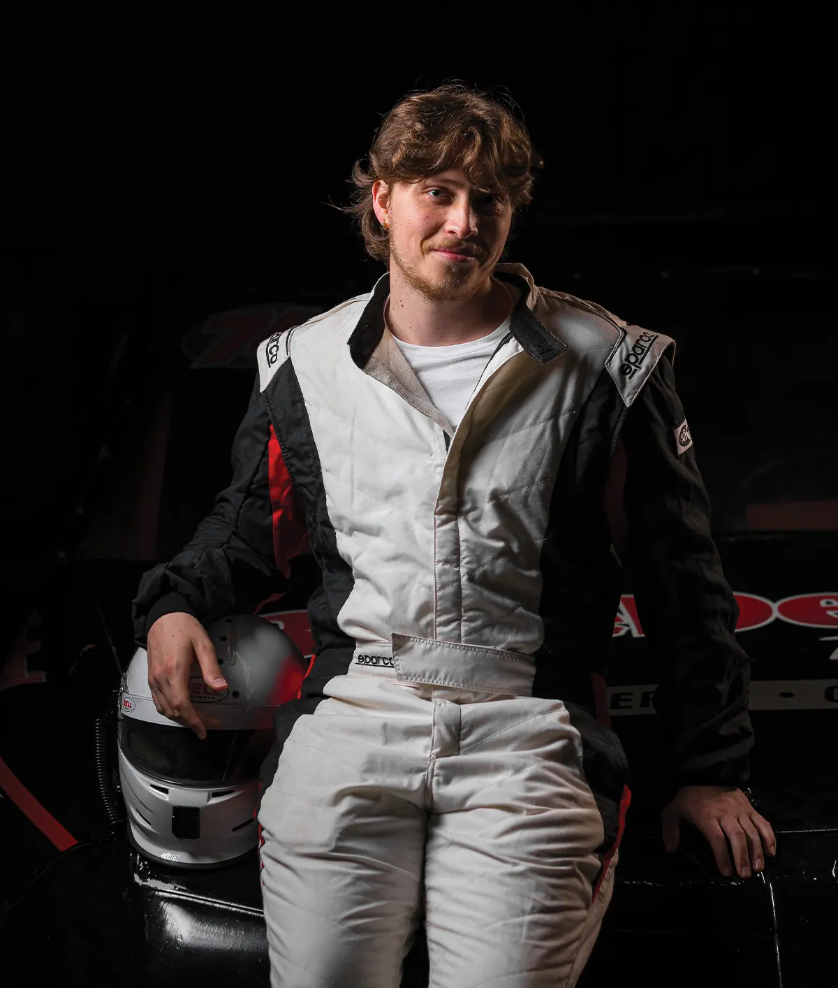 Shane Miata wearing a racing suit and posing in front of a car
