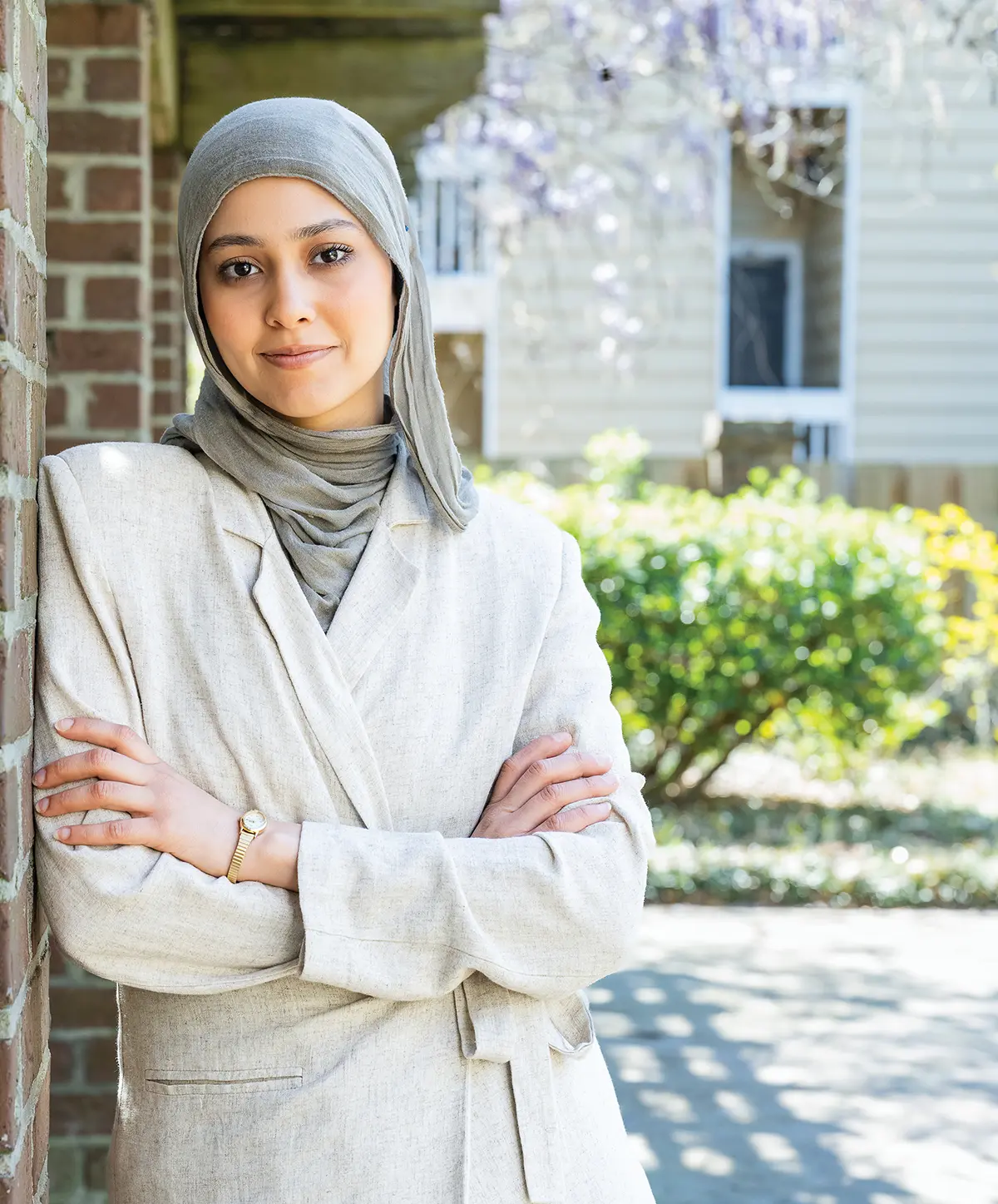 Menatalla "Mena" Shalaby wearing a cream blazer and gray hijab while posing outdoors with her arms crossed