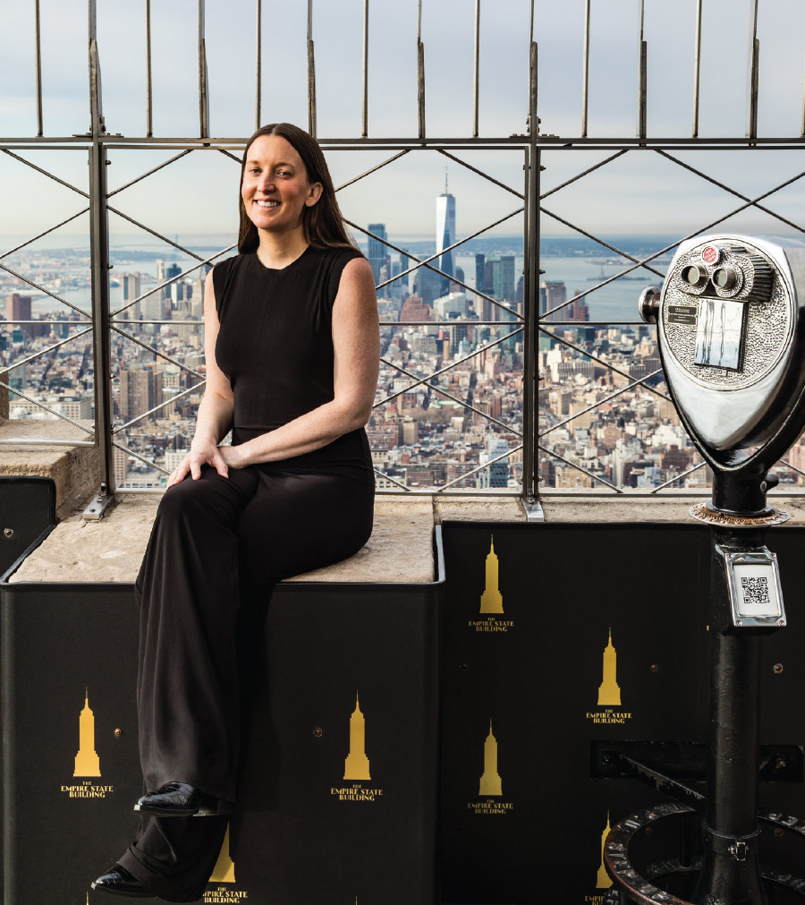 Abby Rickards at the top of the Empire State Building with the skyline behind her