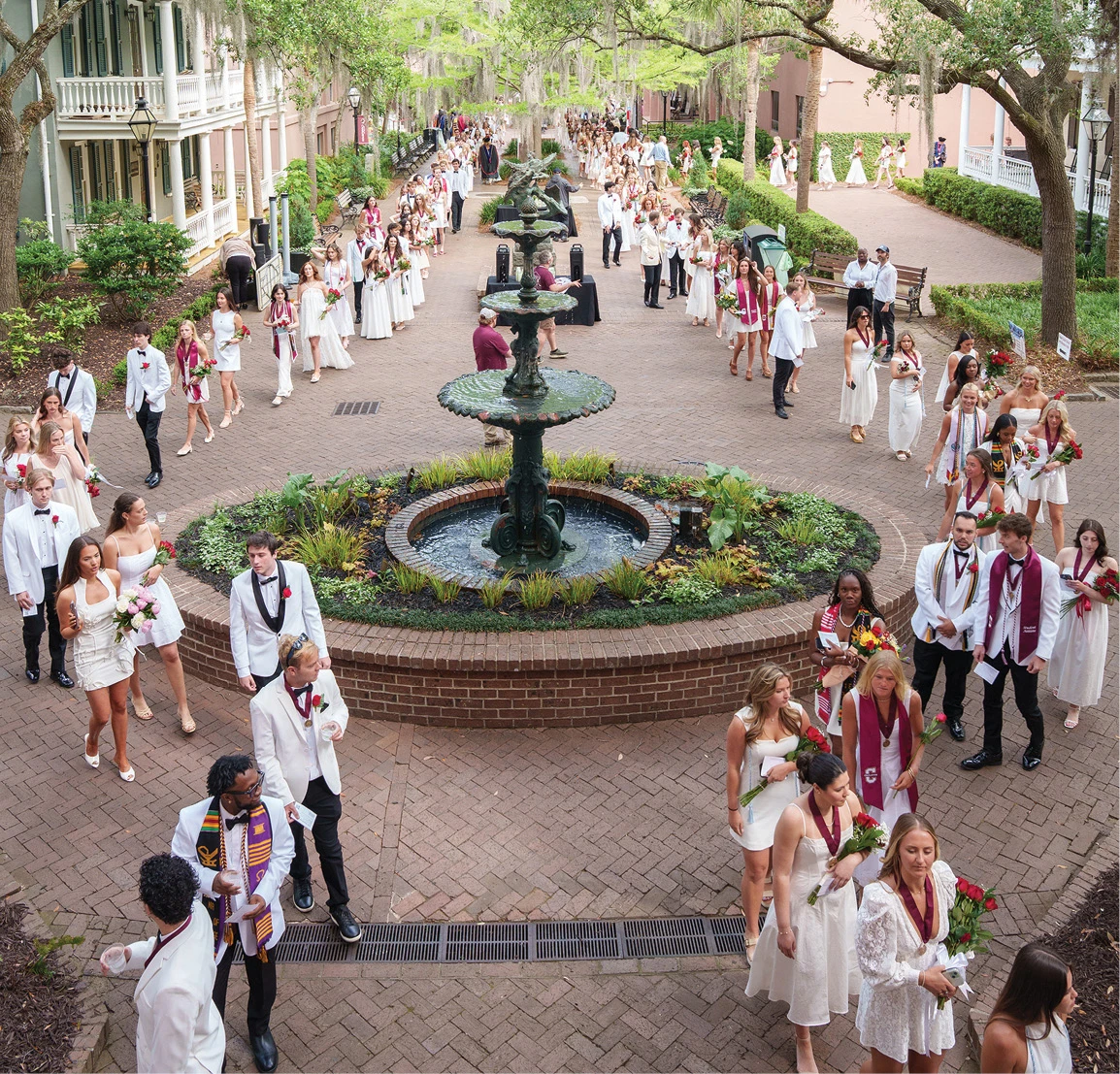 Graduates walking around a courtyard fountain during commencement.