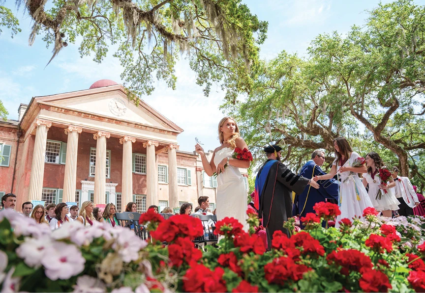 Graduate holding roses in front of a historic campus building during commencement.