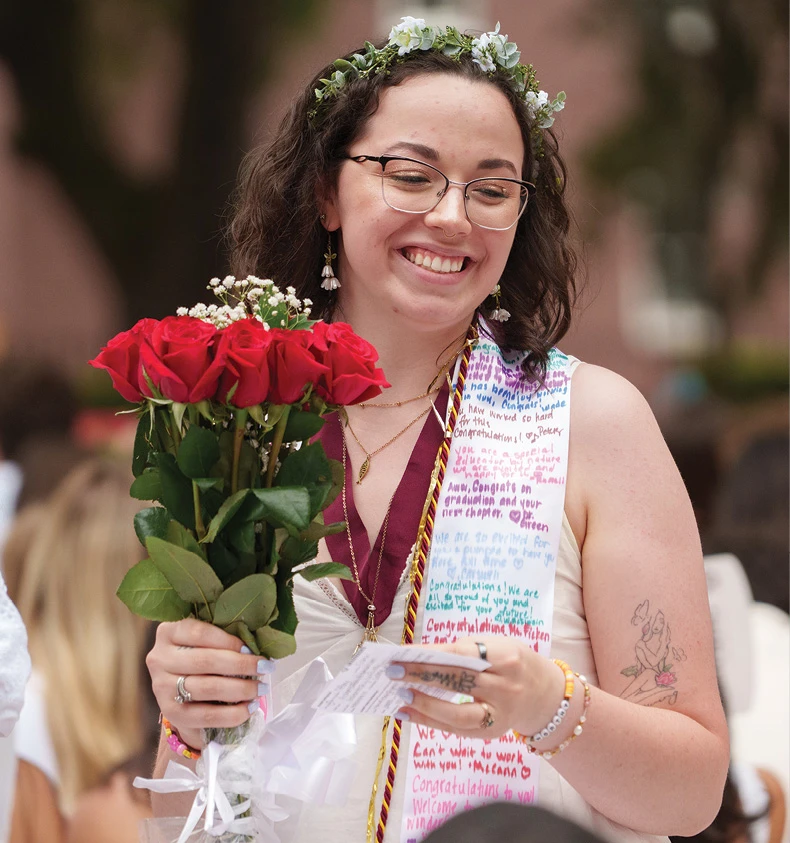 Graduate smiling while holding red roses and commencement cards.