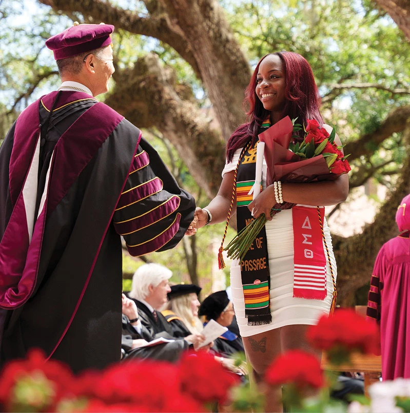 Graduate holding roses and shaking hands with a faculty member during commencement.