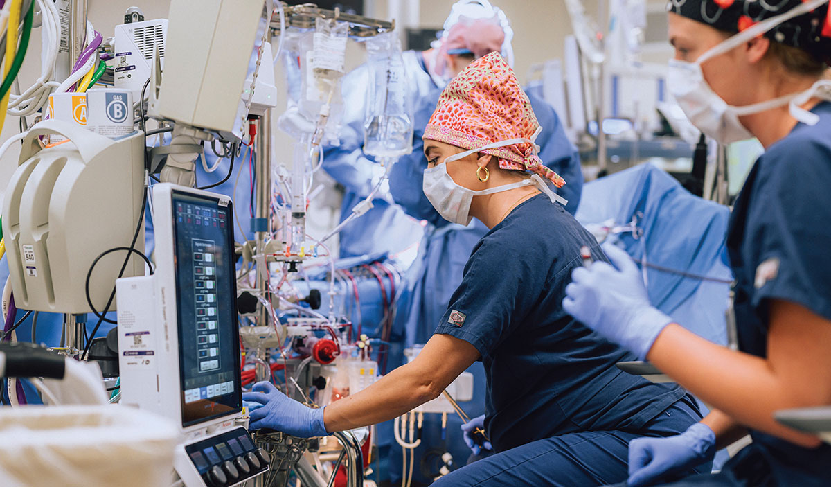 Perfusionist monitoring a heart-lung machine and medical equipment inside a busy operating room.