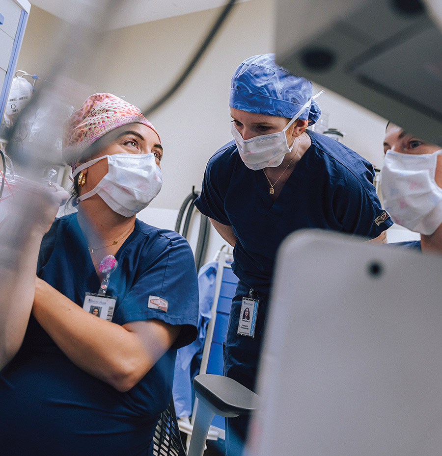 Three healthcare workers wearing surgical caps and masks consulting together in a hospital room.