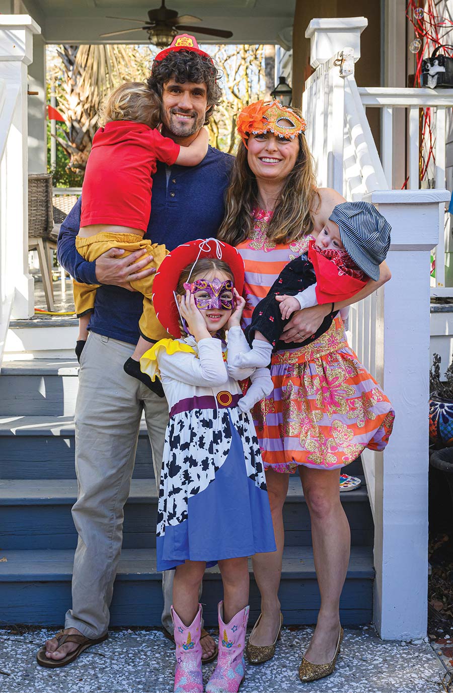 A smiling family of five wearing fun costumes poses together on front porch steps.