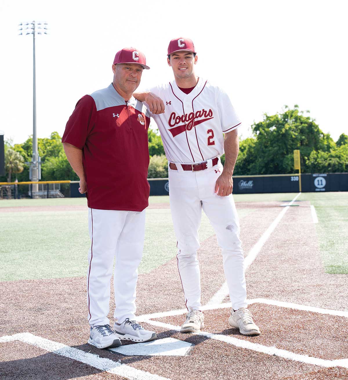 Baseball player Reece Holbrook leaning on his coach and father, Chad Holbrook, on the field.