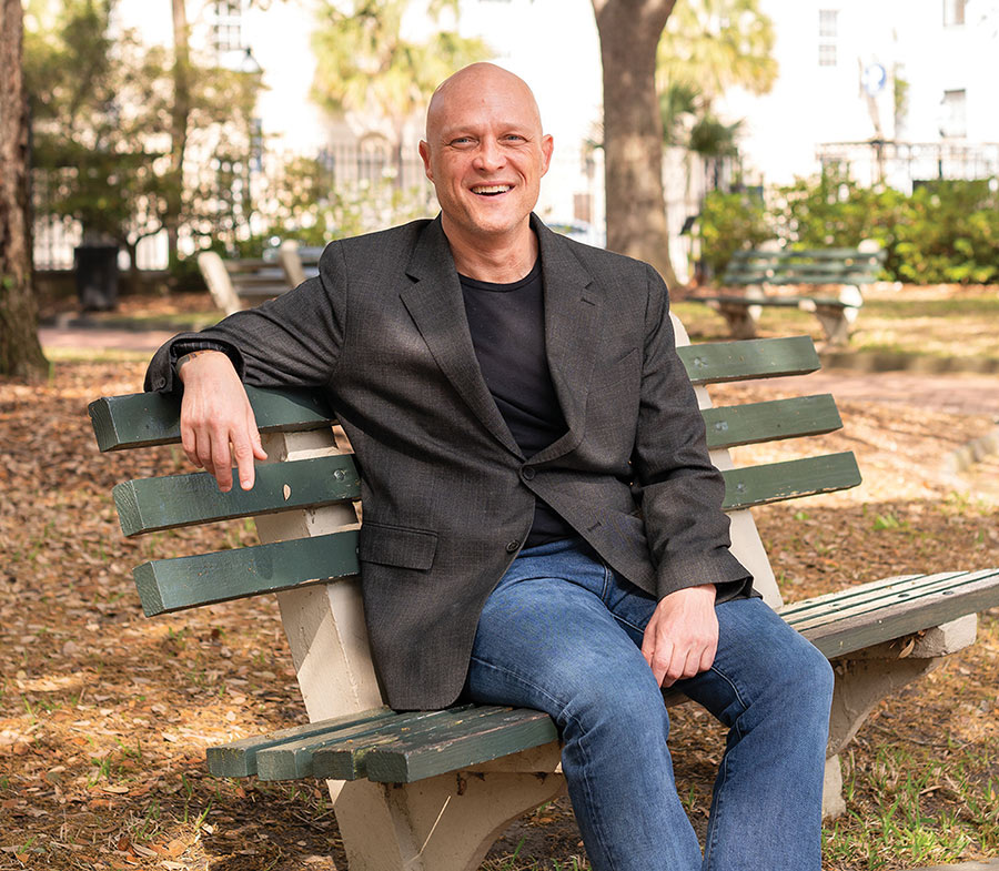 Thomas Nadelhoffer sitting on a bench in a gray coat and jeans